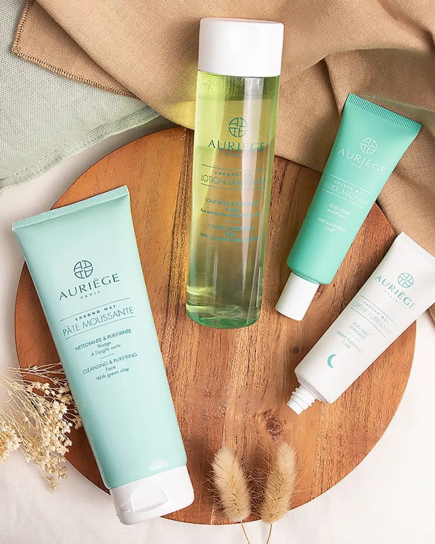 Quatre soins Auriège de la gamme Chrono Mat posés sur une planche en bois : pâte moussante, lotion matifiante, fluide matifiant jour et crème purifiante nuit