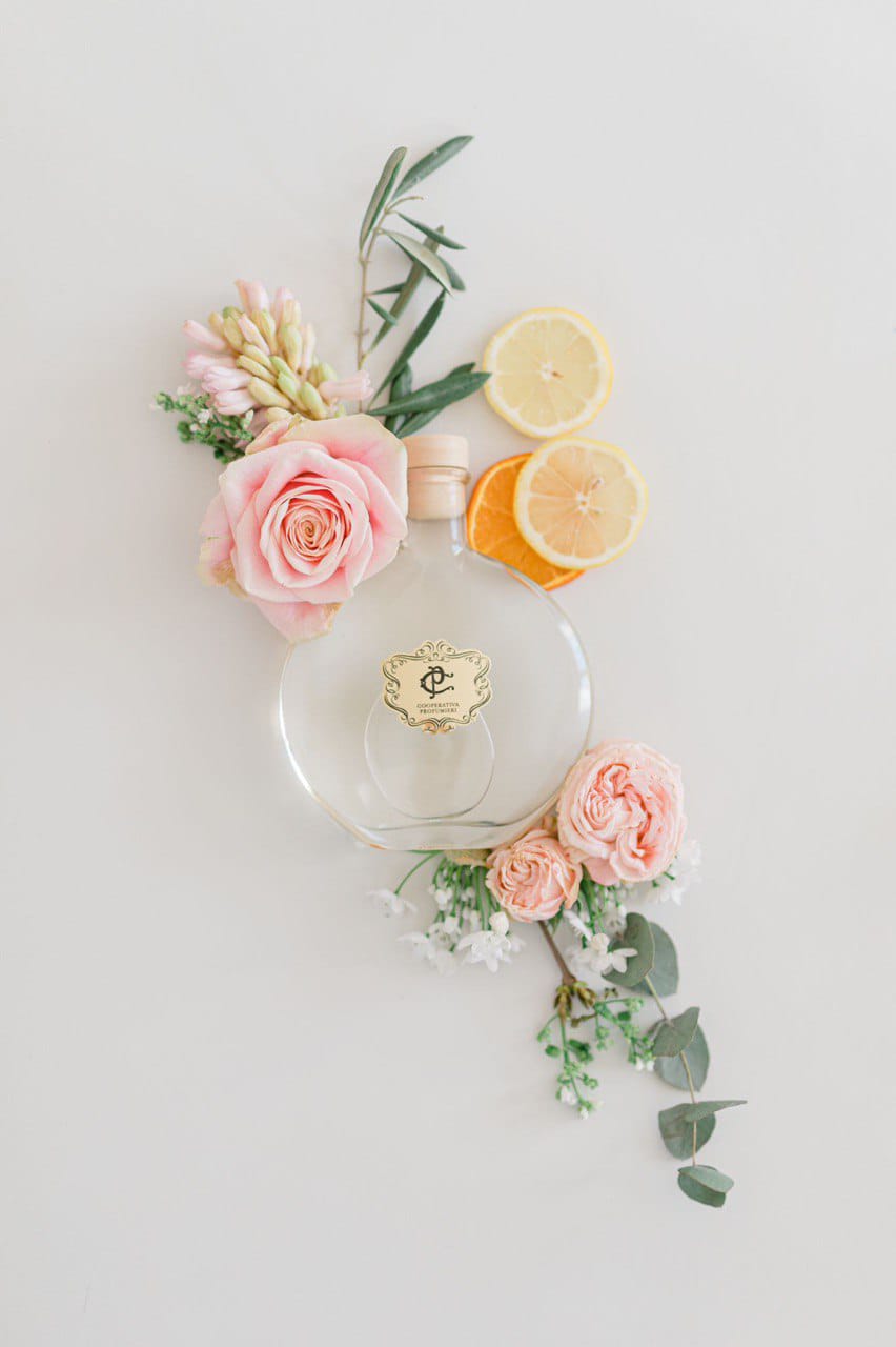 Flacon rond Cooperativa Profumieri entouré de roses, d’agrumes et d’eucalyptus